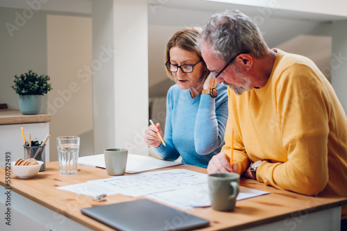 Senior couple sitting at table and looking into blueprints of their new home