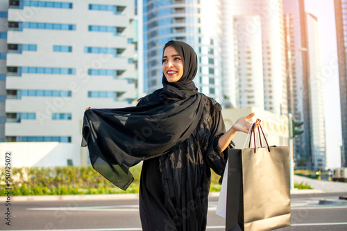 Young beautiful Arabic woman wearing abaya and holding a shopping bags while walking on street. photo