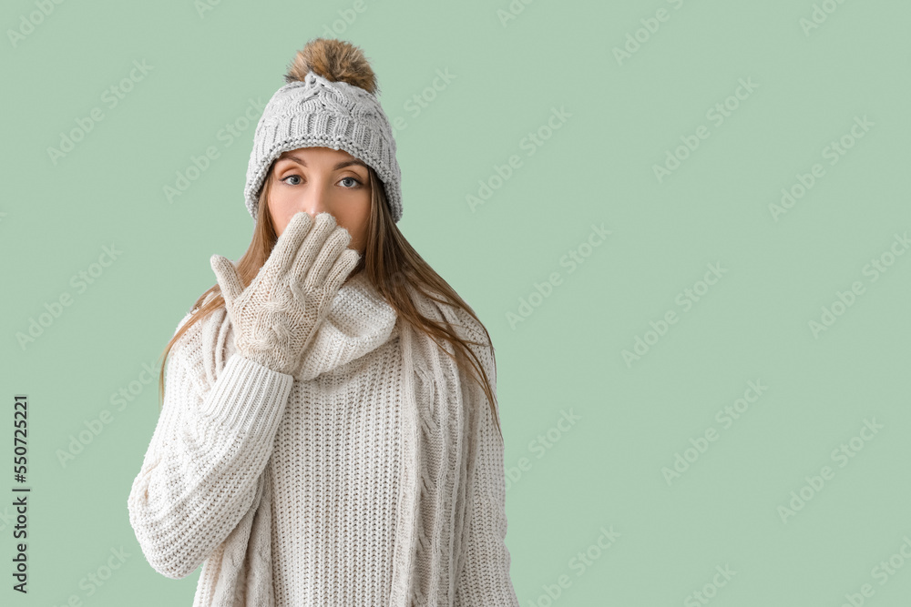 Shocked young woman in warm hat and scarf on green background