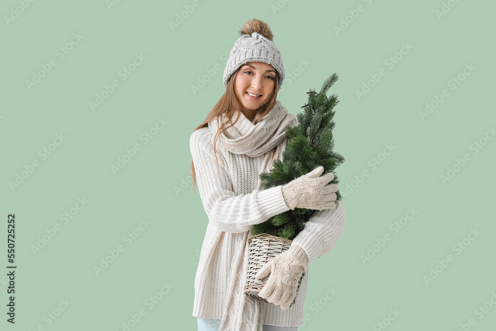 Young woman in warm hat with Christmas tree on green background Young woman in warm hat with Christmas tree on green background