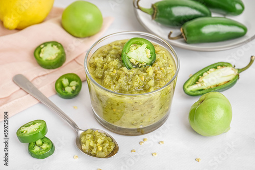 Bowl of tasty green salsa sauce and jalapeno peppers on light background