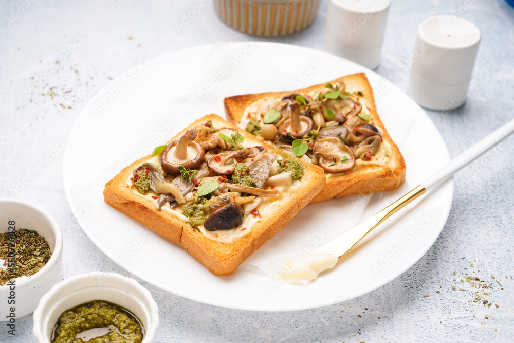 Plate of tasty toasts with cream cheese, mushrooms and pesto sauce on light table