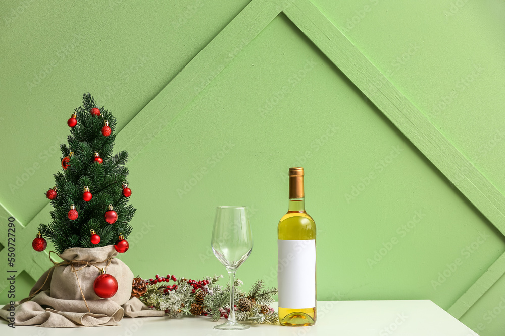 Small Christmas tree with glass and bottle of wine on table near green wall Small Christmas tree with glass and bottle of wine on table near green wall