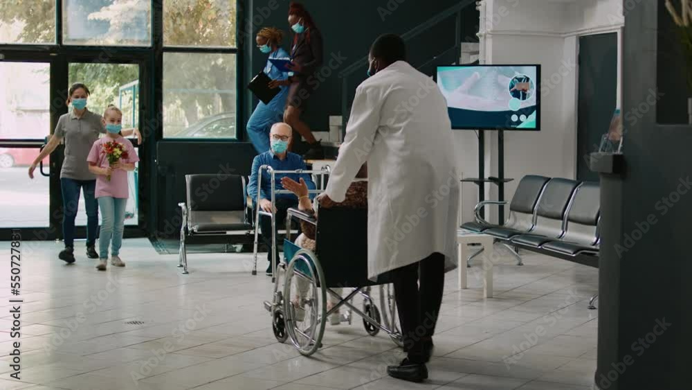 Small child and mother visiting elderly patient at facility, bringing flowers to woman in wheelchair. Child coming to see senior adult with impairment in medical health center, coronavirus. Small child and mother visiting elderly patient at facility, bringing flowers to woman in wheelchair. Child coming to see senior adult with impairment in medical health center, coronavirus.