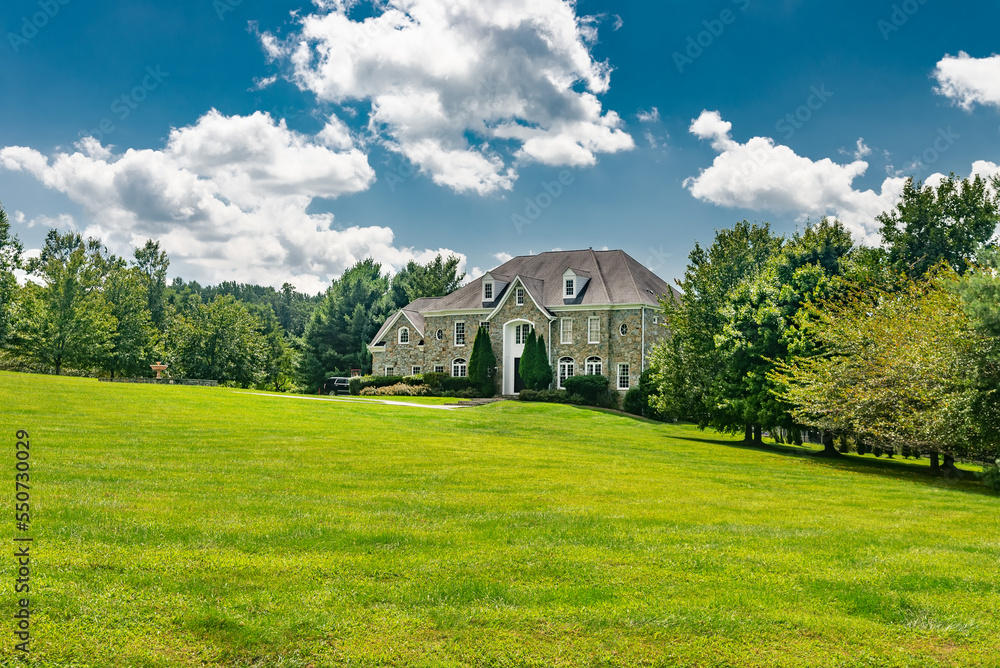 Large traditional American single family home on a large wooded lot in Virginia. Summer landscape on sunny day under cloudy sky.