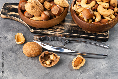 Various nuts in a wooden bowl on gray table and a nut cracker. Close-up of a walnut. Space for text.