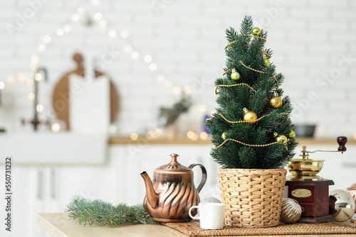 Small Christmas tree with teapot and coffee grinder on table in kitchen