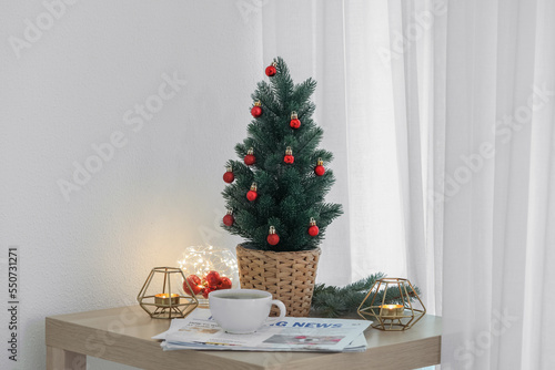 Small Christmas tree, coffee cup, newspapers and candles on table in living room