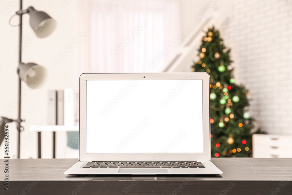 Fototapeta premium Laptop on table against blurred Christmas tree in office