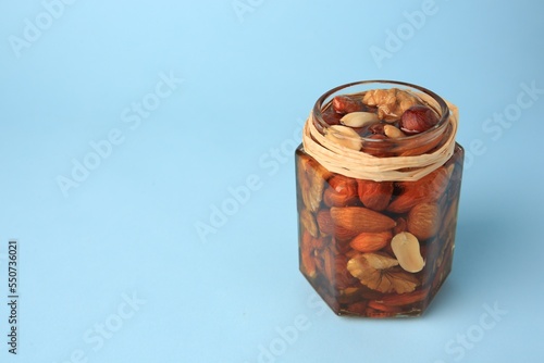 Jar with different delicious nuts and honey on light blue background. Space for text