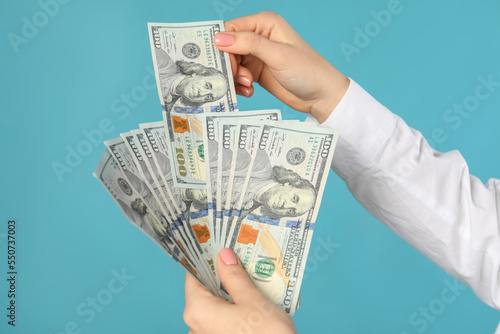 Woman holding dollar banknotes on turquoise background, closeup. Money exchange concept