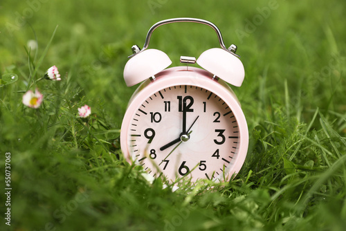 Pink alarm clock on green grass outdoors, closeup