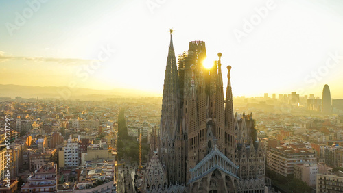 Closeup aerial view of the Sagrada Familia cathedral in Barcelona, Spain. Cathedral is in shadow with the sun rising behind cathedral between two spires.