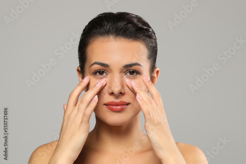 Woman applying cream under eyes on grey background. Skin care