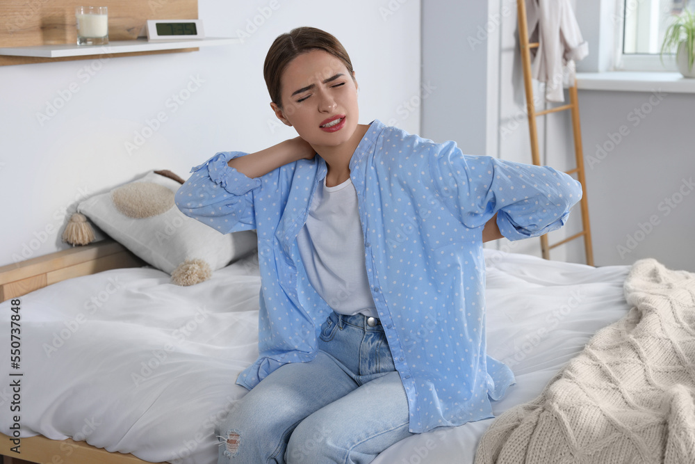 Woman suffering from back pain while sitting on bed at home. Symptom of scoliosis Woman suffering from back pain while sitting on bed at home. Symptom of scoliosis