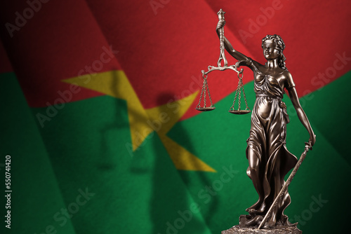 Burkina Faso flag with statue of lady justice and judicial scales in dark room. Concept of judgement and punishment, background for jury topics photo