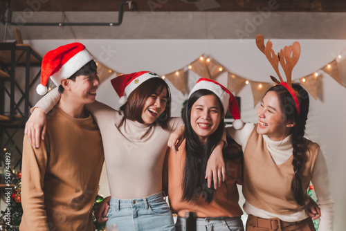 Group of young Asian man and women as friends having fun at a New Year's celebration, hugging singing laughing at a midnight countdown Party at home with Christmas tree decoration for holiday season.