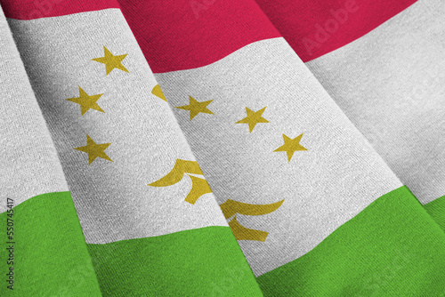 Tajikistan flag with big folds waving close up under the studio light indoors. The official symbols and colors in fabric banner photo