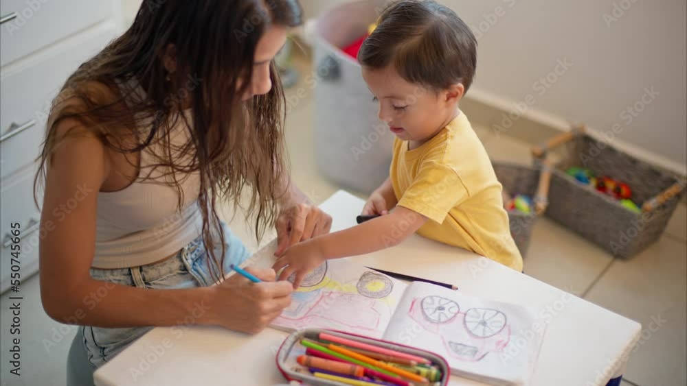 Young little latin toddler wearing a yellow t-shirt with his mom drawing colorful cars and trucks on a white notebook. Mother teaching his son how to draw. Young little latin toddler wearing a yellow t-shirt with his mom drawing colorful cars and trucks on a white notebook. Mother teaching his son how to draw.