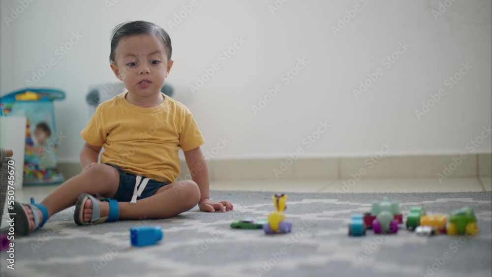 Young cute latin toddler sitting on the floor on a grey carpet making faces and talking to the camera
