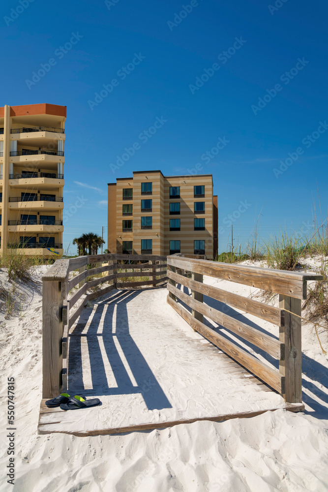 Sand covered wood pathway with handrails near the buildings against the clear blue sky at Destin, FL Sand covered wood pathway with handrails near the buildings against the clear blue sky at Destin, FL