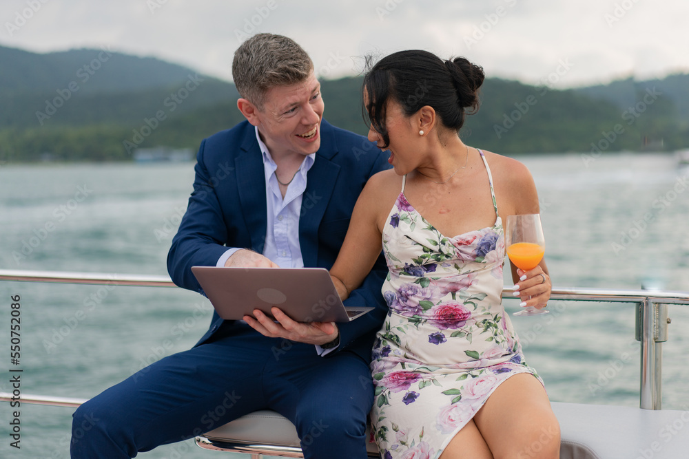 Caucasian businessman and businesswoman working outdoor together on digital tablet for online corporate. Two luxury business people working with laptop on a sailing boat. Concept business travel