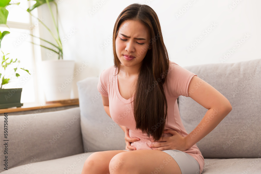 Asian young woman have a stomach pain and feeling unwell on sofa at home. Woman stressed and sick Asian young woman have a stomach pain and feeling unwell on sofa at home. Woman stressed and sick