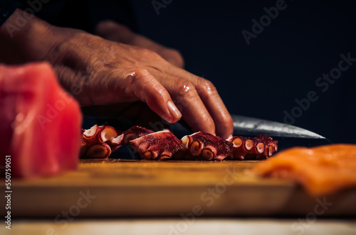 Close up of Chef cook hands chopping octopus for traditional Asian cuisine with Japanese knife. Professional Sushi chef cutting seafood japanese chefs are making octopus sashimi. Dark Tone