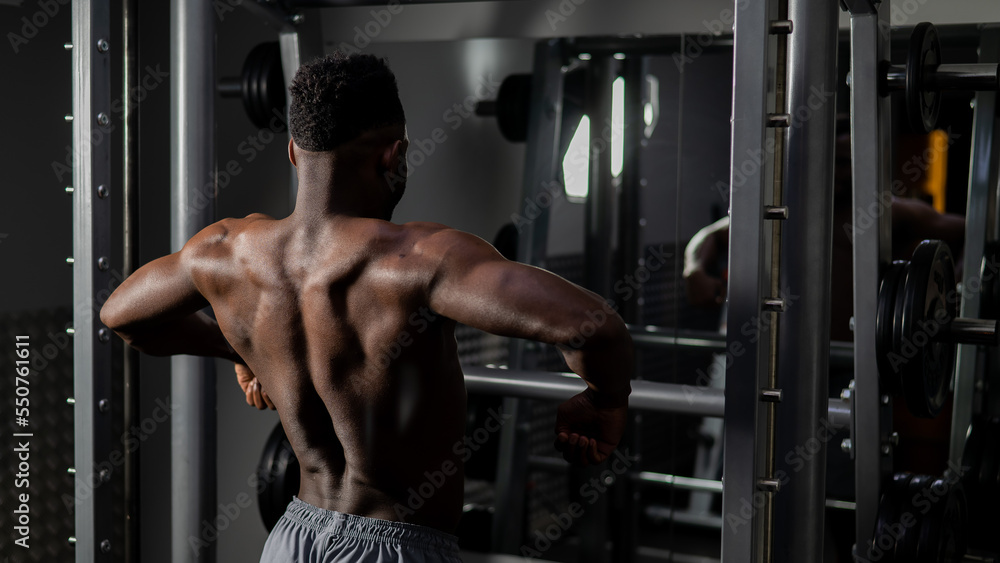 Naklejka premium Handsome afro american man posing showing back muscles in gym.