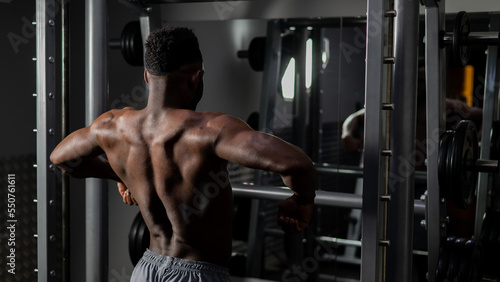 Handsome afro american man posing showing back muscles in gym. 