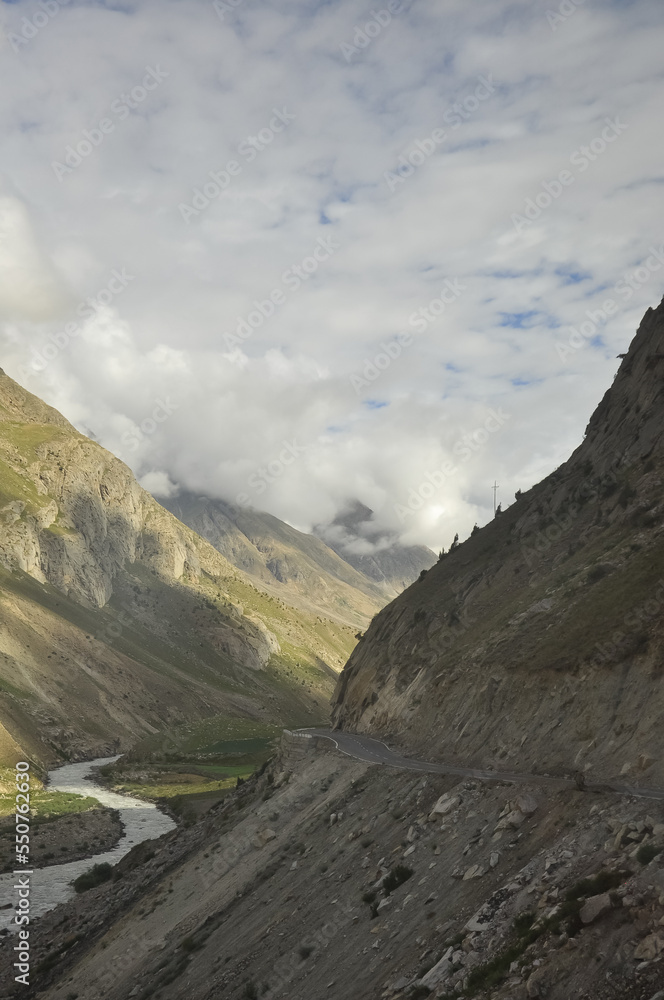 View of narrow cliffside mountain road with flowing a river in between dry mountains in Manali-Leh highway