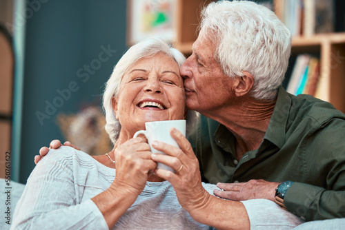 Coffee kiss, love and senior couple smile for retirement, conversation and relax in the living room of a house. Home tea, affection and elderly man and woman with comic communication in the lounge