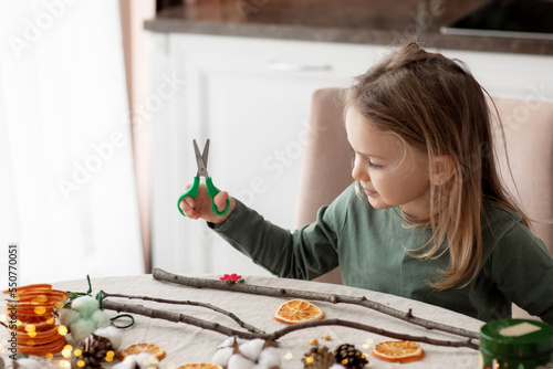 Winter holiday season. child little toddler girl making handmade Christmas garland home decorations from natural ECO materials