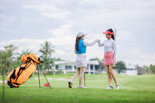 two asian women golfers congratulate high-five and happy smiling at golf course, with the golf bag next to them,