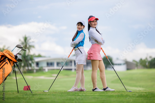 Two young asian women professional golfers stand and pose looking at camera and smiling taking photo at the golf course,