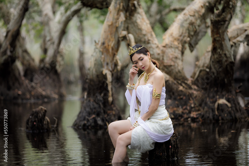 beautiful  Thai asian woman in white dress local tradition costume in the name is Nakee, sitting on tree stump in the lake in the botannical garden rayong thailand,  photo