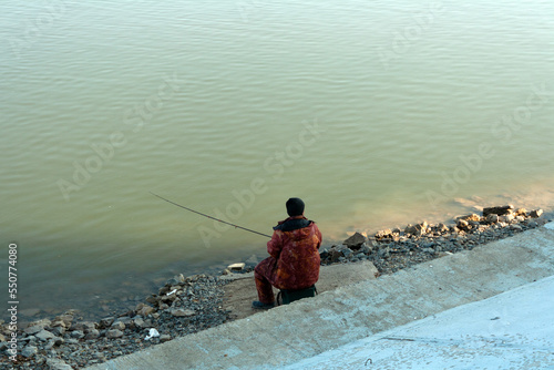 a man with a fishing rod is sitting on the river bank