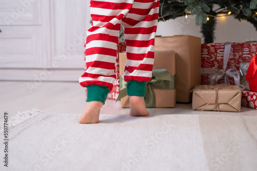 close up kid legs in Christmas pajamas near gift boxes and Christmas tree