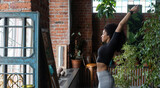 Slim Afro-American woman stretching at home or fitness studio in the morning. Studio decorated with plenty house plants, big windows and brick wall. Concept of happy and conscious healthy lifestyle.