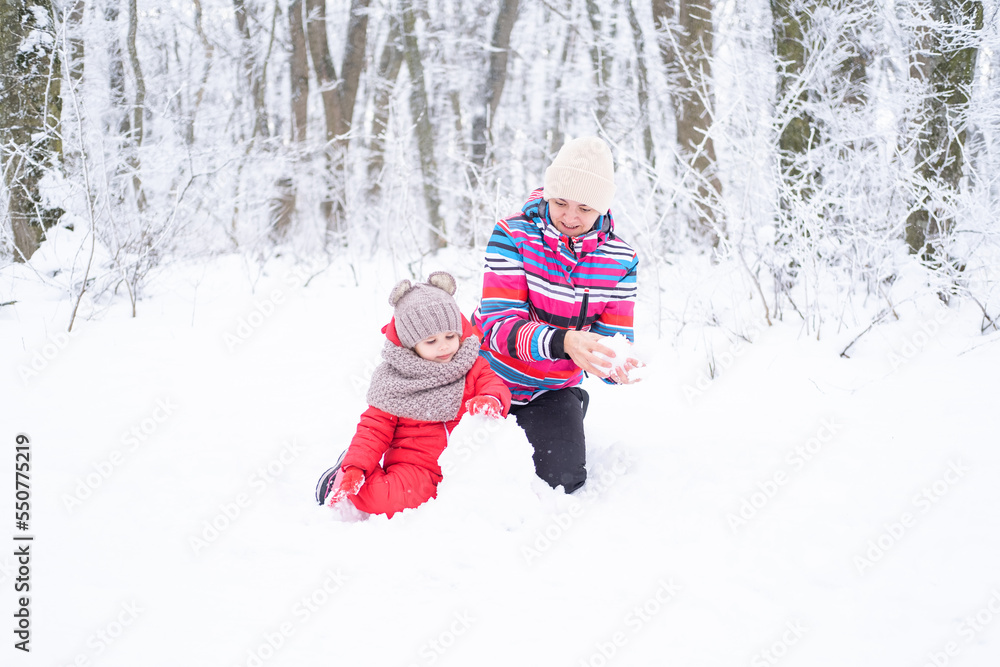 Mother and daughter on winter walk in nature. woman and child girl make snowman