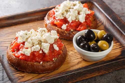 Cretan dakos is for a traditional salad from the island of Crete consists of barley rusk topped with juicy tomatoes, cheese and olive oil closeup on the wooden board on the table. Horizontal