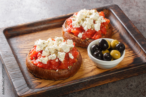 Obraz na plátně Dakos consists of a slice of cracked barley bread and garnished with crushed or grated ripe tomato and crumbled feta with oregano and olives closeup on the wooden board on the table