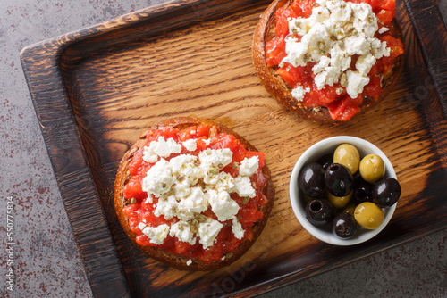 Cretan dakos is for a traditional salad from the island of Crete consists of barley rusk topped with juicy tomatoes, cheese and olive oil closeup on the wooden board on the table. Horizontal top view  photo