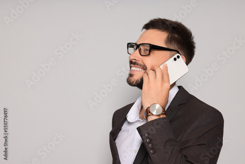 Handsome man in suit talking on smartphone against light grey background. Space for text