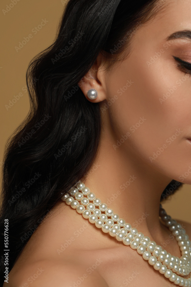 Young woman wearing elegant pearl jewelry on brown background, closeup