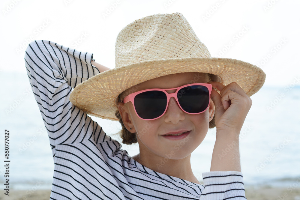 Little girl wearing sunglasses and hat at beach on sunny day