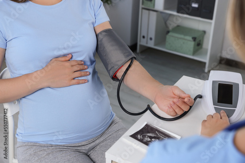 Doctor measuring blood pressure of pregnant woman in hospital, closeup