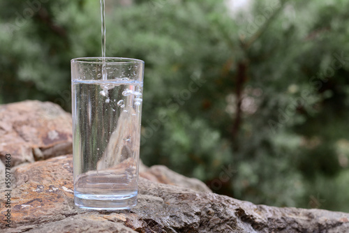 Pouring pure water into glass on stone outdoors, space for text