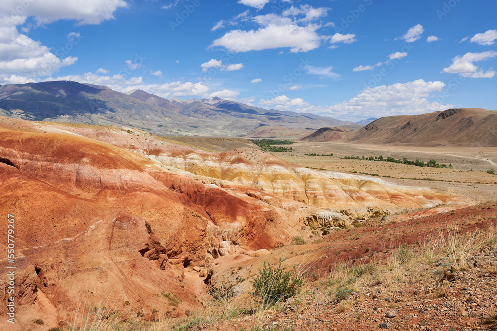 Picturesque sunny view of a valley with colorful hills against a blue sky with clouds in the sunlight. Beautiful mountain scenery, colorful mountains in sunlight. Picturesque sunny view of a valley with colorful hills against a blue sky with clouds in the sunlight. Beautiful mountain scenery, colorful mountains in sunlight.