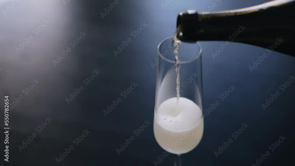 The wine from the bottle is poured into a glass standing on the table. The camera takes a close-up The wine from the bottle is poured into a glass standing on the table. The camera takes a close-up